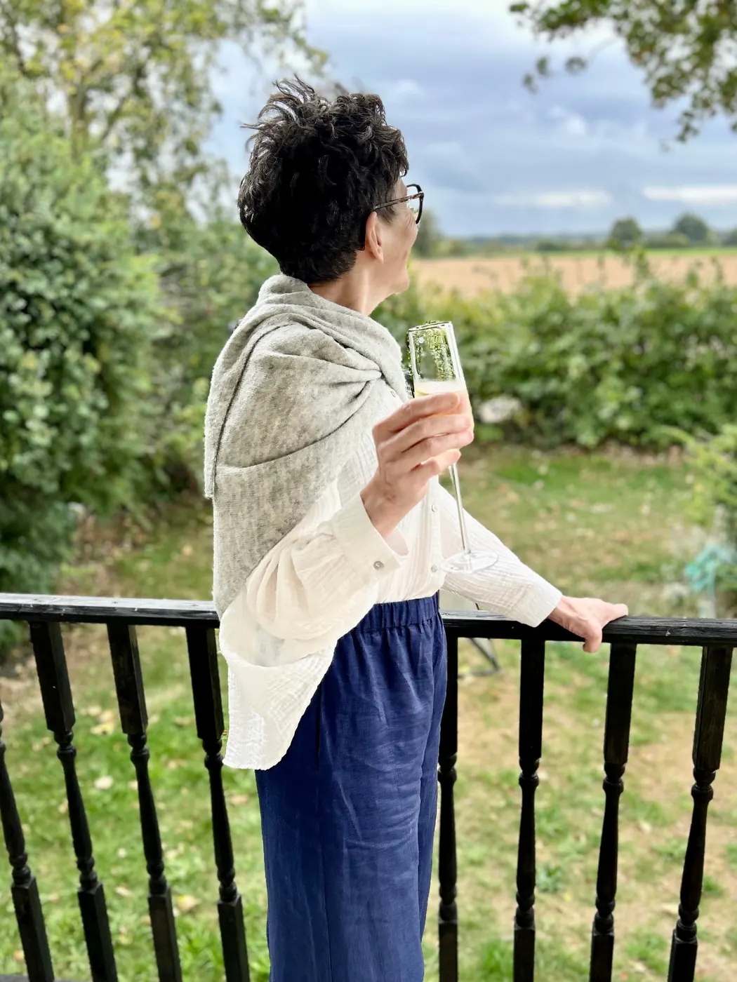 Isobel outdoors in a white linen shirt, blue trousers and grey wrap