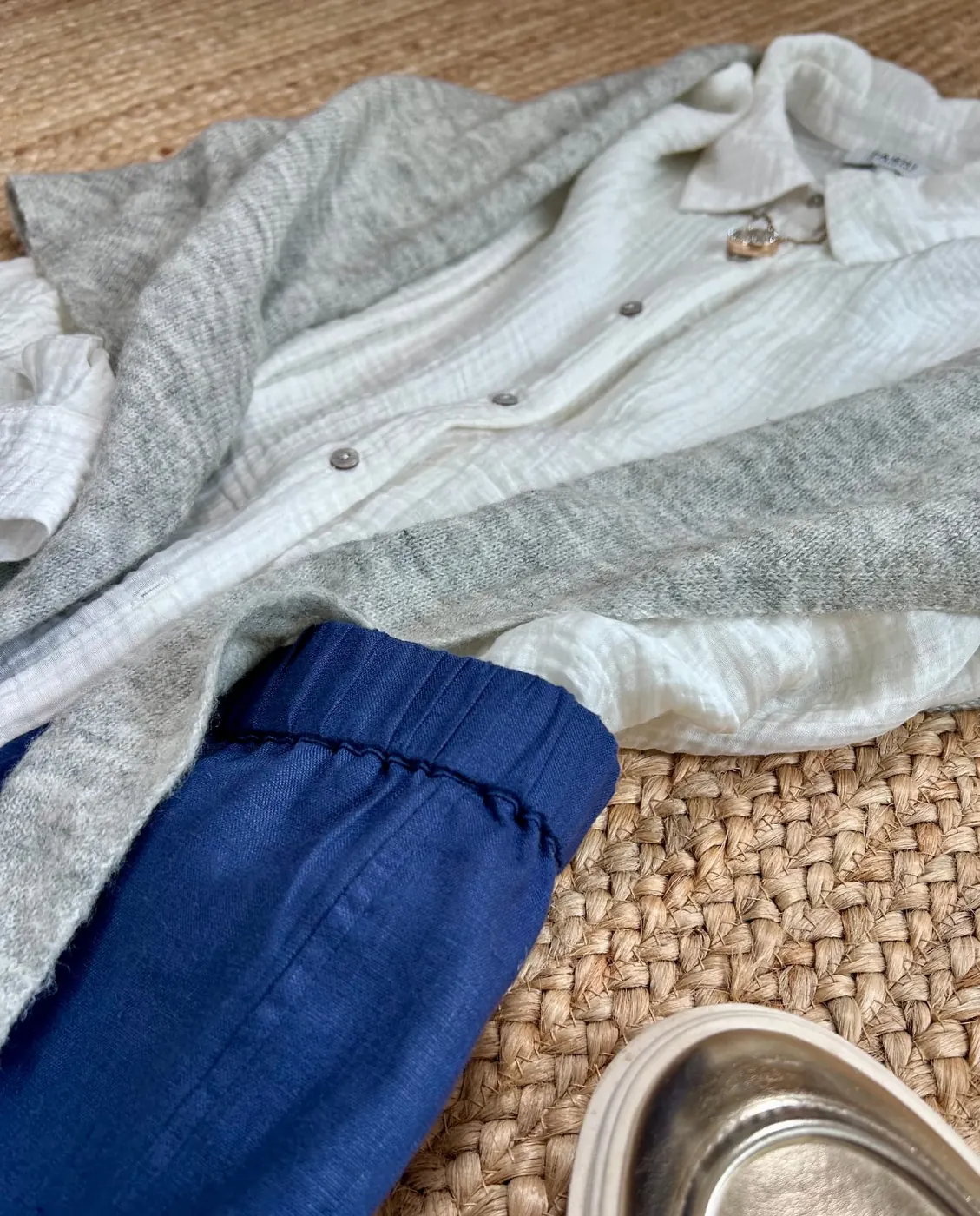 Detail of the grey cardigan, white shirt, blue trousers and gold shoe